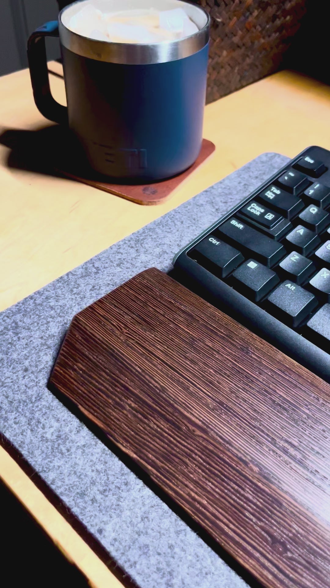 A video of a desk setup with a wenge wrist rest showcased with a black keyboard on a charcoal wool felt and cork desk pad.