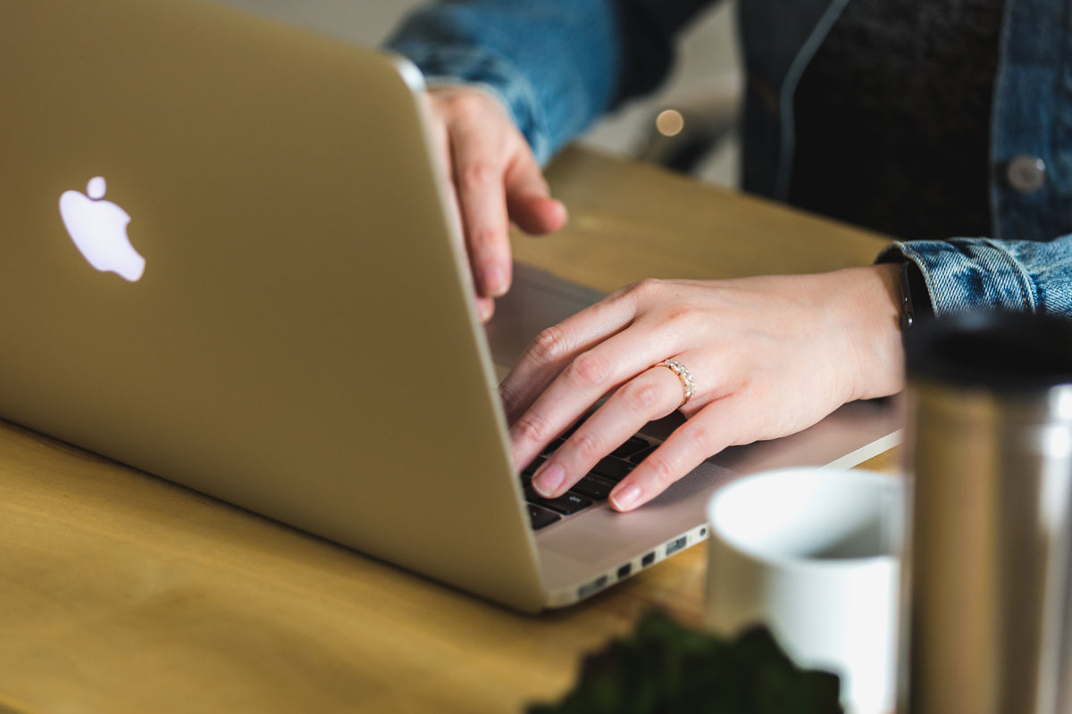 Looking from the back of a silver Macbook laptop showing hands with a diamond ring typing.