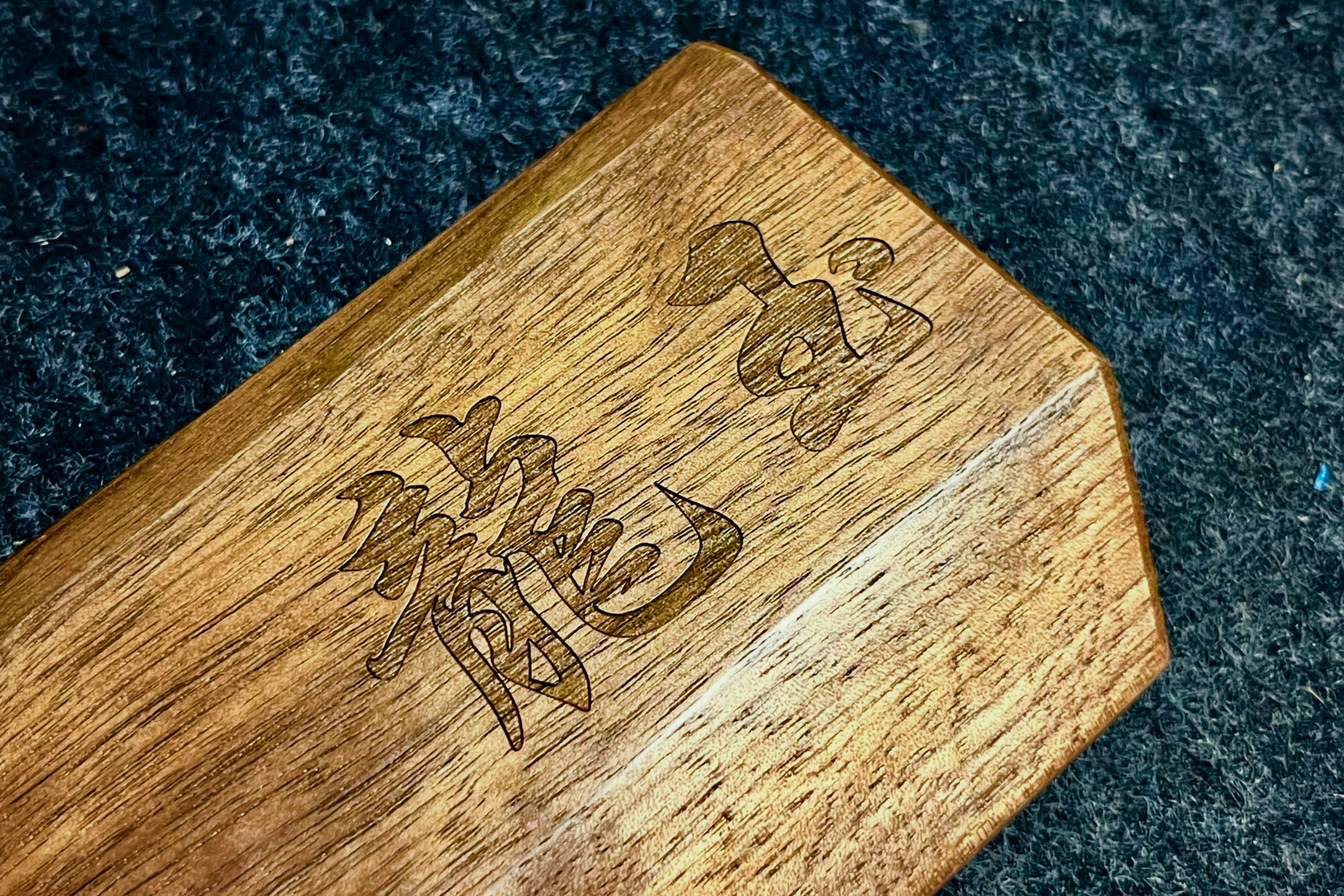 A close-up of a Lonoke Designs walnut mechanical keyboard wrist rest with engraved Chinese characters, resting on a dark textured surface.