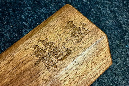 A close-up of a Lonoke Designs walnut mechanical keyboard wrist rest with engraved Chinese characters, resting on a dark textured surface.